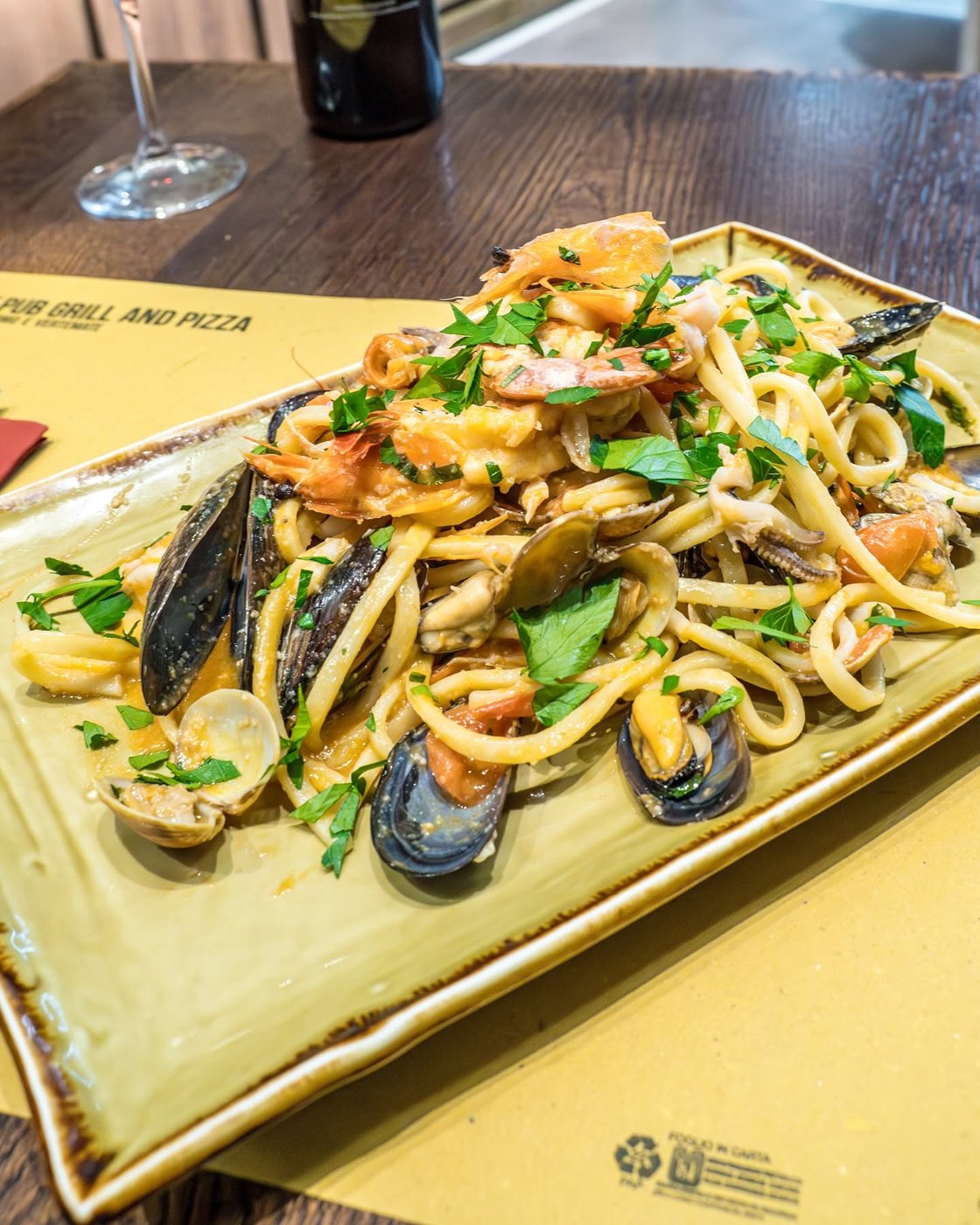 Linguine allo scoglio di OX Como con cozze, vongole, gamberi e prezzemolo su piatto rettangolare in ceramica verde