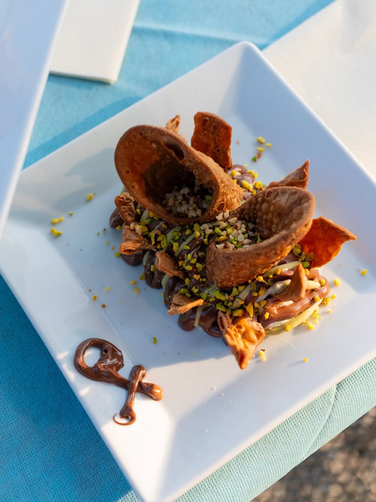 Cannolo scomposto di OX Como: cialde croccanti su crema al cioccolato e granella di pistacchio, piatto quadrato bianco